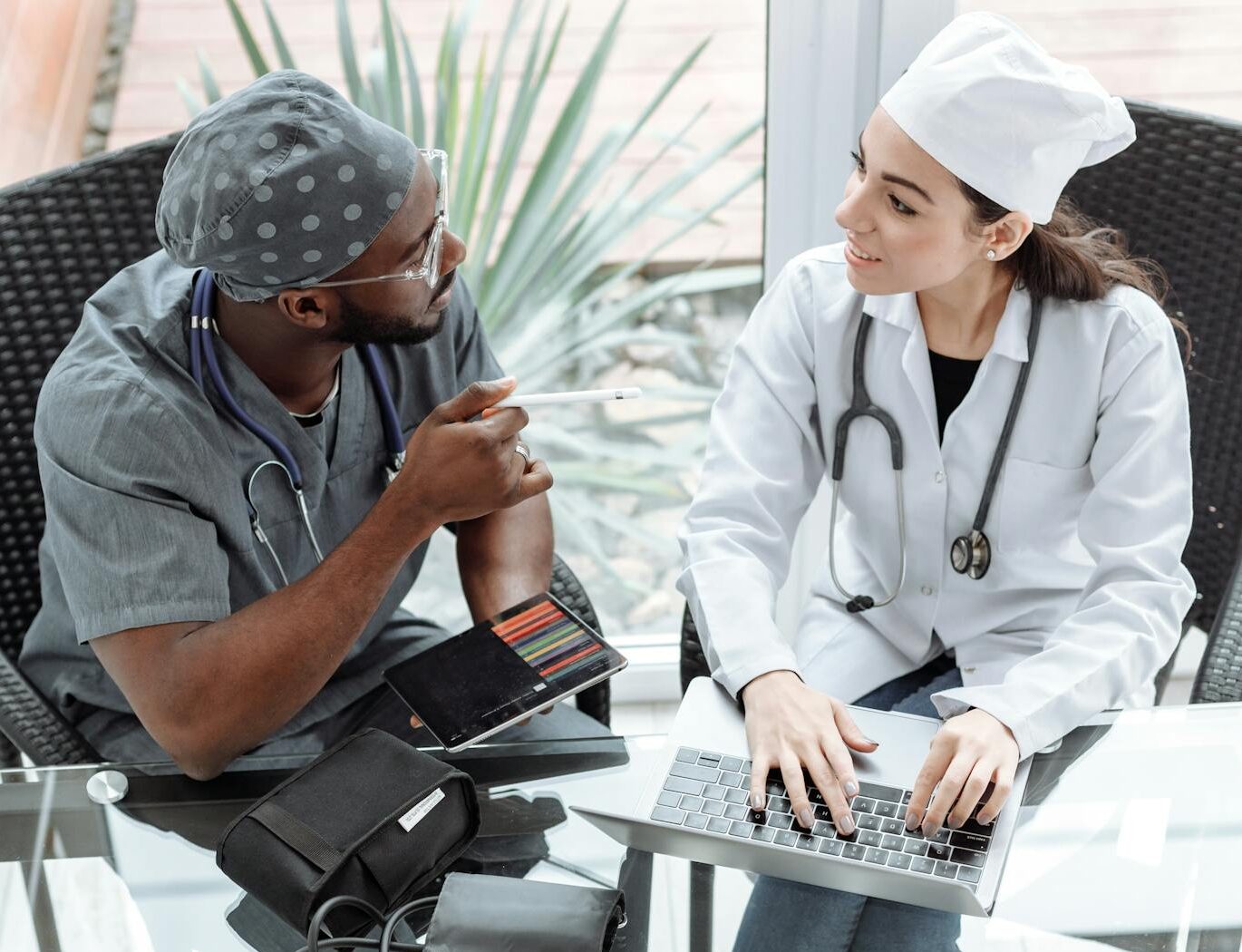 Two doctors discussing patient care using a laptop and tablet indoors.
